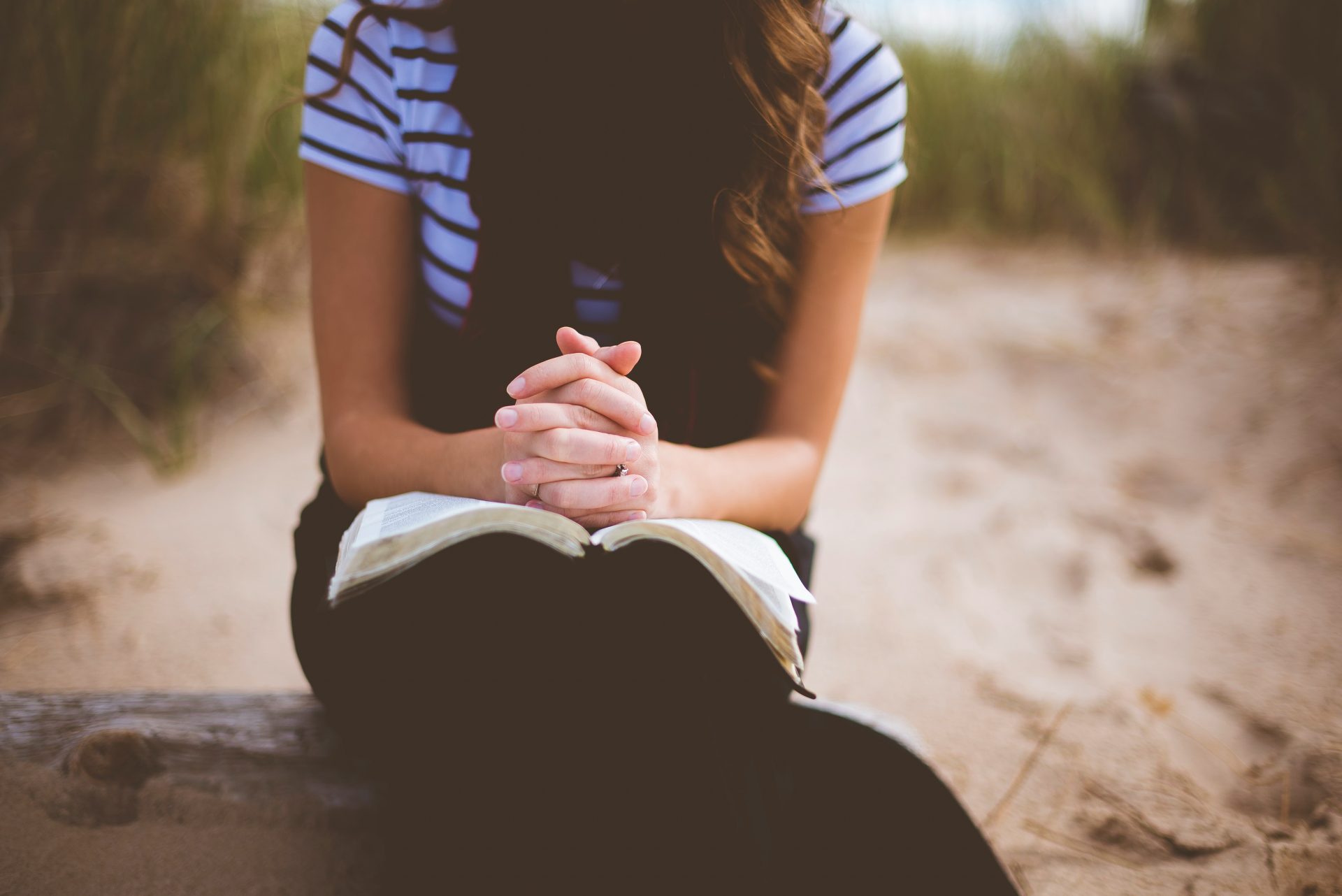 Woman sitting outdoors, praying with Bible.