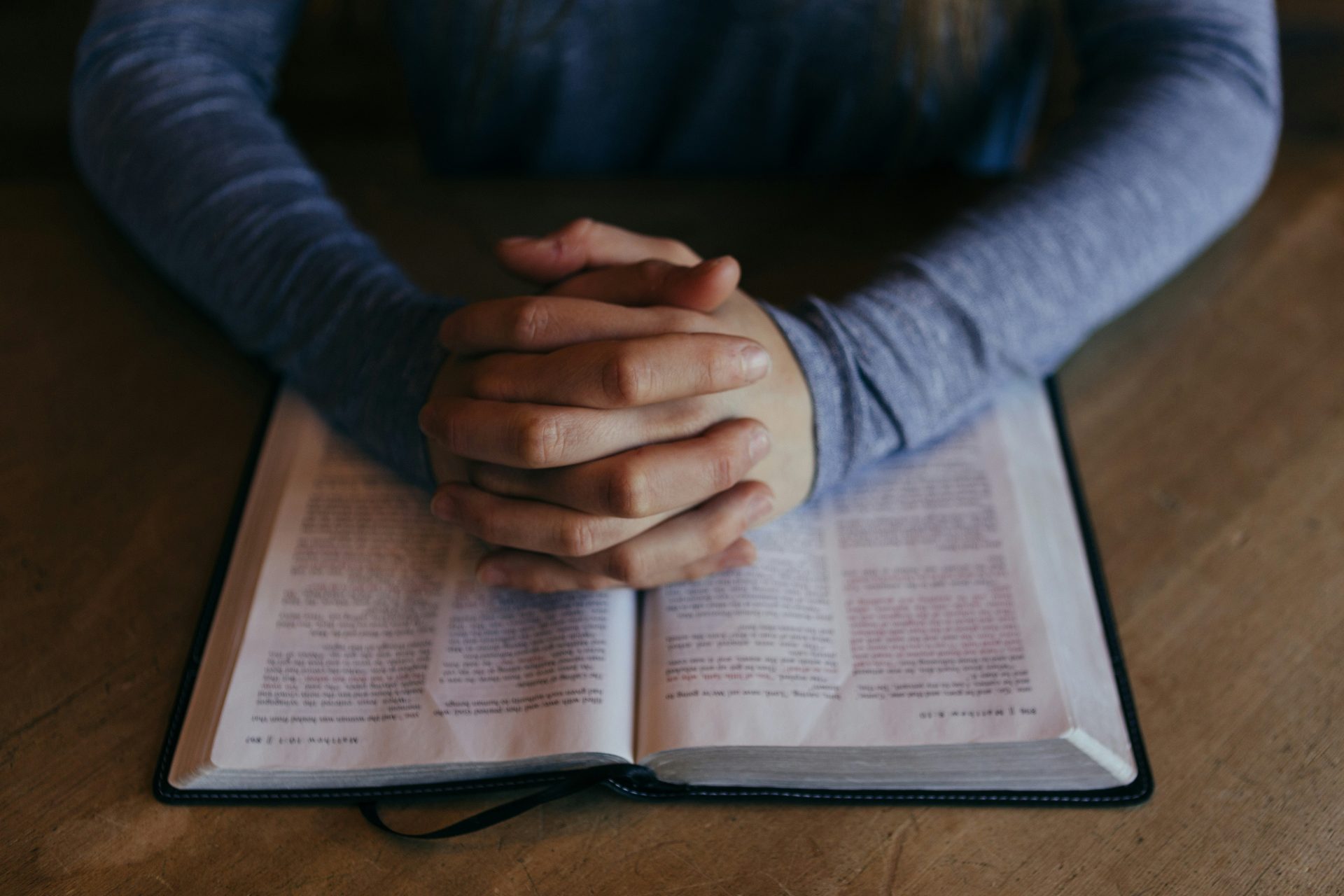 Hands clasped on an open Bible.