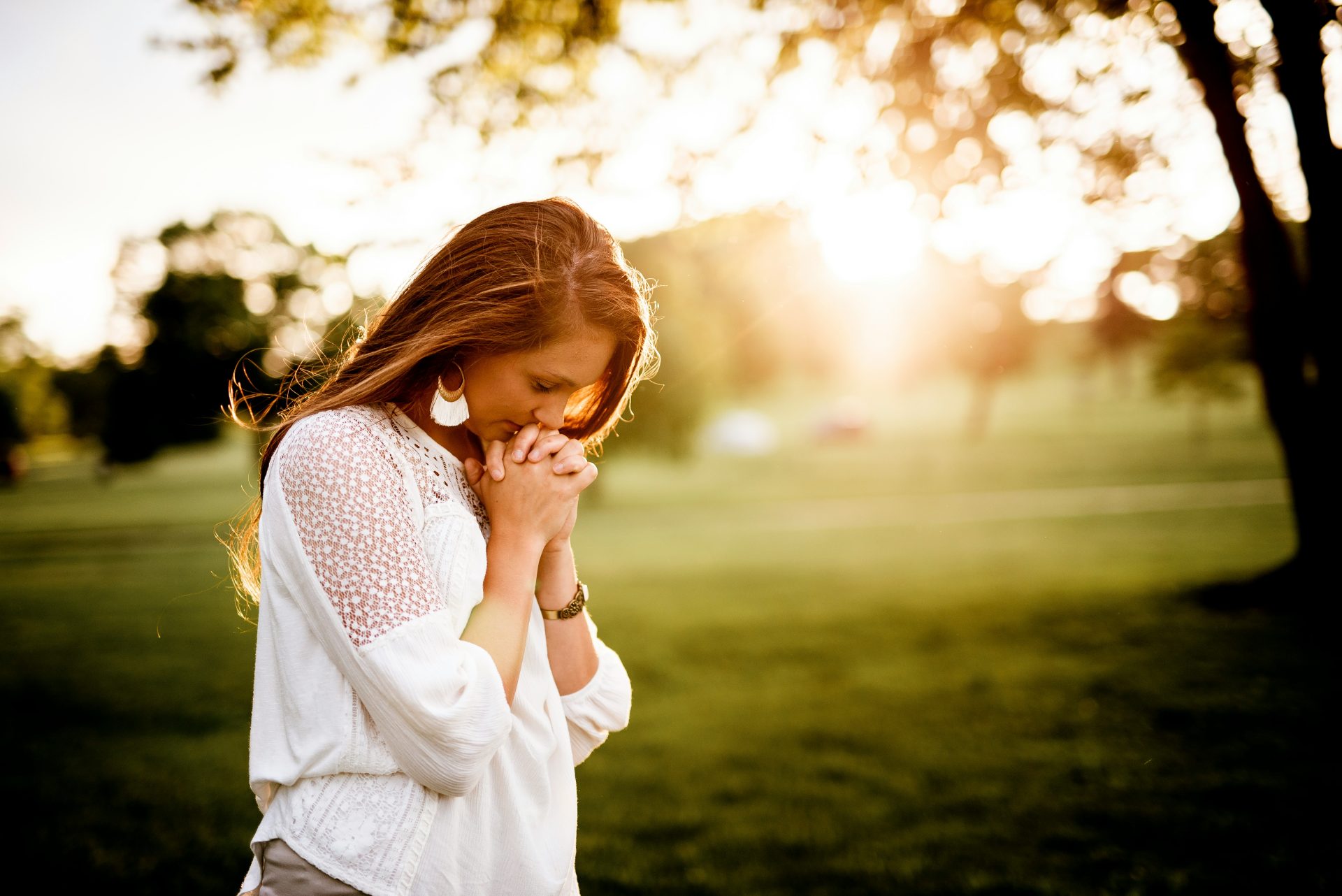 Woman praying outdoors at sunset, peaceful.